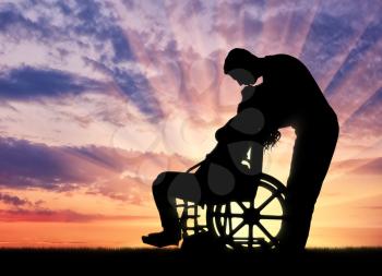 Silhouette of a man kissing a disabled woman in a wheelchair at sunset