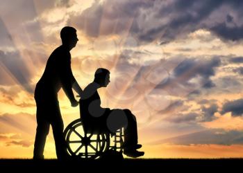 Silhouette of a disabled man in a wheelchair and a nurse in the sunset. The concept of caring for people with disabilities
