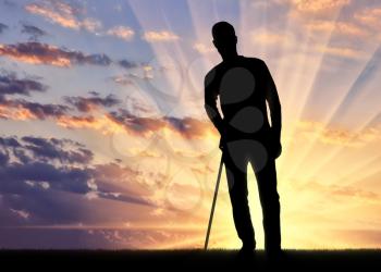 Silhouette of a disabled man supports himself with a crutch against the sunset background. Concept of people in rehabilitation