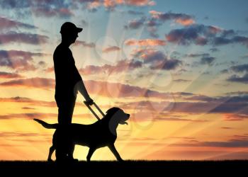 Silhouette of a blind disabled man holding a dog guide against a sunset background. The concept of assistance to blind people with disabilities