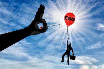 A selfish businessman clings to a balloon called the ego and a big hand with a needle intends to burst it. Conceptual scene the higher you fly the harder they fall