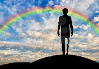 Disabled person with a prosthetic leg standing on the hill on a background of clouds and rainbow