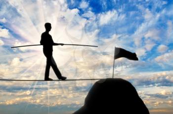 The concept of balance and equilibrium in the business. Silhouette of a businessman walking toward the target on the tight rope
