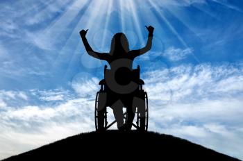 Silhouette of a happy disabled woman in a wheelchair on top of a hill. The concept of happy people with disabilities
