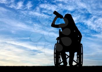 Silhouette of a disabled woman in a wheelchair drinking water from a plastic bottle. Concept of leisure and recreation for disabled people