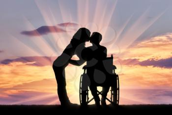 Silhouette of a disabled man in a wheelchair and his wife who is kissing. The concept of caring and supporting disabled people