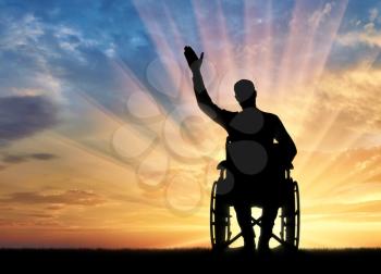 Silhouette of a disabled man in a wheelchair waving his hand. The concept of people with disabilities