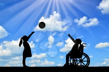 Silhouette of a disabled child girl in a wheelchair and healthy girl playing in a ball outdoors. The concept of children with disabilities in a society of healthy children