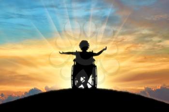 Silhouette of a happy disabled child girl sitting in a wheelchair atop a hill at sunset. Concept of happy children with disabilities