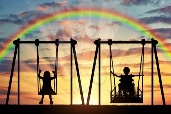 Happy child is a disabled person in a wheelchair riding an adaptive swing next to a healthy child together. Concept of adaptive equipment for children with disabilities