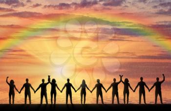 Silhouette of a group of happy people holding hands by the sea at sunset with a rainbow. The concept of mutual assistance and support in people