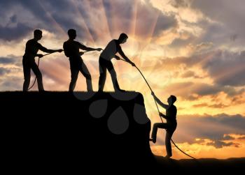 Silhouette of three men help to climb up another man. The concept of teamwork and mutual assistance