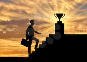 A silhouette of a businessman climbs the stairs to the trophy. Business concept leader