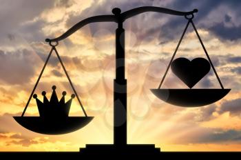 The silhouette of the scales which bowl is inclined towards the crown, not the heart, against the background of the sunset. Concept image of selfishness