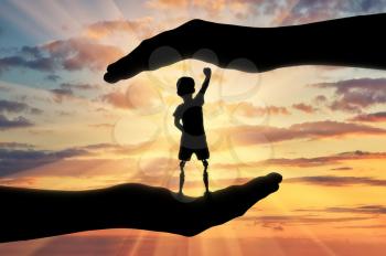 Help children with disabilities concept. Happy disabled boy with a prosthetic leg standing in the helping hands at sunset