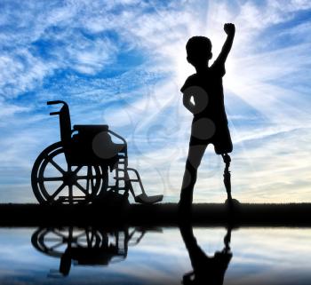 Children with disabilities concept. Happy disabled boy with a prosthetic leg standing near a wheelchair at the river with reflection