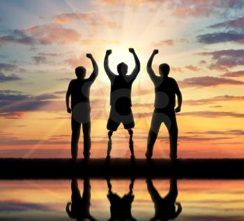 Support for people with disabilities concept. Happy disabled man with a prosthetic leg standing and his friends at sunset by the river with their reflection