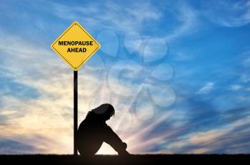 Sad woman sitting in front of a road sign menopause ahead. A conceptual image of a woman's imminent menopause