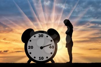 Sad woman standing at the clock hand which shows almost 40 years. Conceptual image of impending menopause in women
