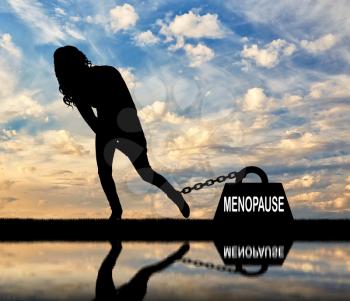 The silhouette of a sad woman and a heavy load of menopause is chained to her leg. Conceptual image of menopause in women