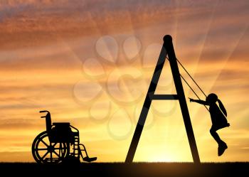 Silhouette of a child disabled girl on a swing next to a wheelchair on a sunset background. Concept of children with disabilities and their leisure