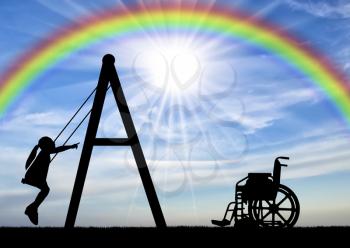 Silhouette of a child disabled girl on a swing next to a wheelchair on a background of the sky with a rainbow. Concept of playing children with disabilities