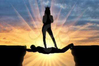 Selfish woman with a crown standing on a man in the form of a bridge over an abyss. Concept of selfishness and personal interest