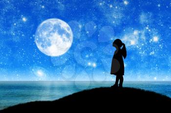 Silhouette, little girl child standing on a hill by the sea looking at the starry sky. Conceptual image of children's dreams