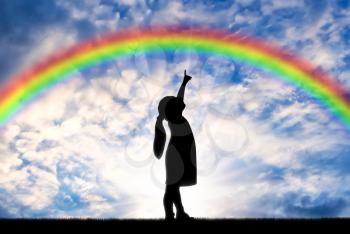 Silhouette of a baby girl showing a finger in the sky on a rainbow. Conceptual childhood scene