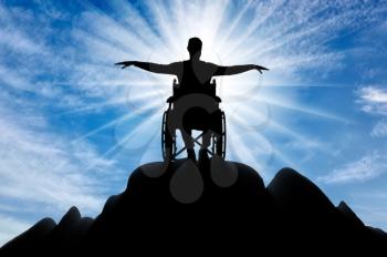 Silhouette of happy disabled man in wheelchair on top of mountain. The concept of happy people with disabilities