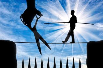 Silhouette of a man balances on a rope over sharp spikes and a hand with scissors intends to prune a rope. Concept of risks in business