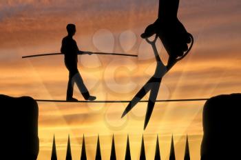 Silhouette of a man balancing on the rope over sharp spikes, and the hand with the scissors means to cut the rope. The concept of a rival in business
