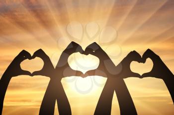 Three pairs of hands show a heart symbol on a sunset background. Altruism concept