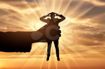 Workplace bullying concept. Silhouette of a man's hand holds a man in a fist on a sunset background.