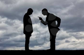 Workplace bullying concept. Silhouette of a boss yelling at a man employee with his head bowed against a cloudy sky