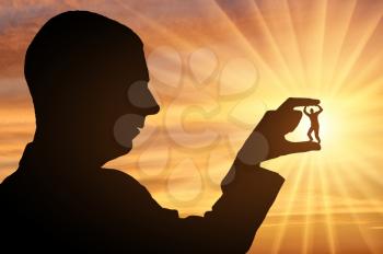 Silhouette of a man holds a man between his fingers on a sunset background. Workplace bullying concept