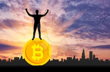 Happy man standing on a coin bitcoin against the background of the city. The concept of success in the crypto currency