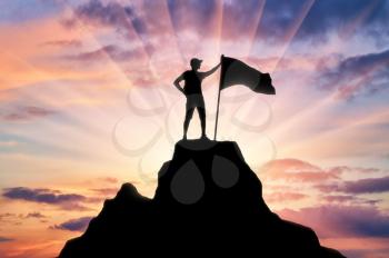 Silhouette of a climber with a flag on the top of the mountain which he subdued. Conceptual Scene