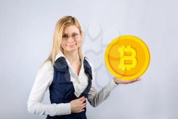 A woman in glasses holds a bitcoin in her hand. The concept of crypto currency