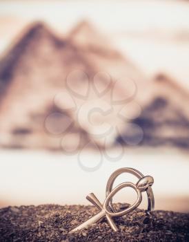 The Egyptian ankh is a cross in the sand against the backdrop of the Great Pyramids. Photo toned.