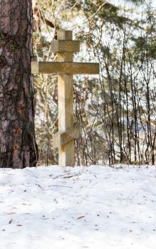 A commemorative Orthodox cross on a hill in the snow among the pines.