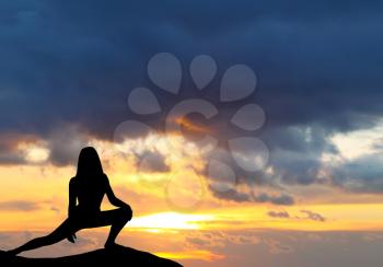 Silhouette of woman practicing yoga during sunset at the seaside.