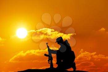Silhouette shot of soldier holding gun with colorful sky and mountain in background