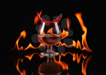 Hot chili pepper in a  cognac ballon with a fire on a black background