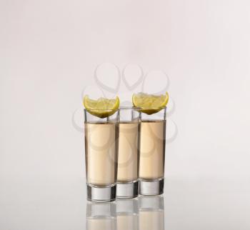 Three gold tequila shots with lime  on white background