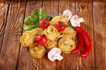 pasta on the wooden background with tomato, pepper, olive oil, mushrooms and lettuce top view 