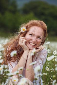 Young lovely smiling woman wonders on flower, tearing petals, close-up.