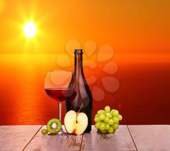 glass of red wine, a bottle of wine and grapes apple on board isolated on white background