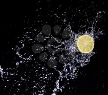 Half a lime falling into the water isolated on a black background