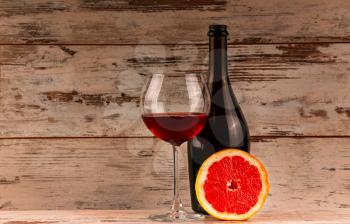 Red wine in glass with bottle and grapefruit on wooden background